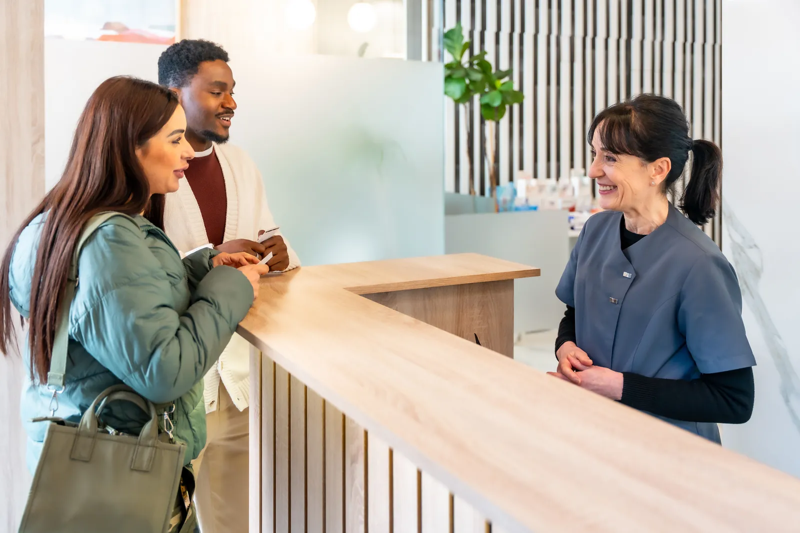 Two patients filling out paperwork at a dental practice reception desk with a staff member
