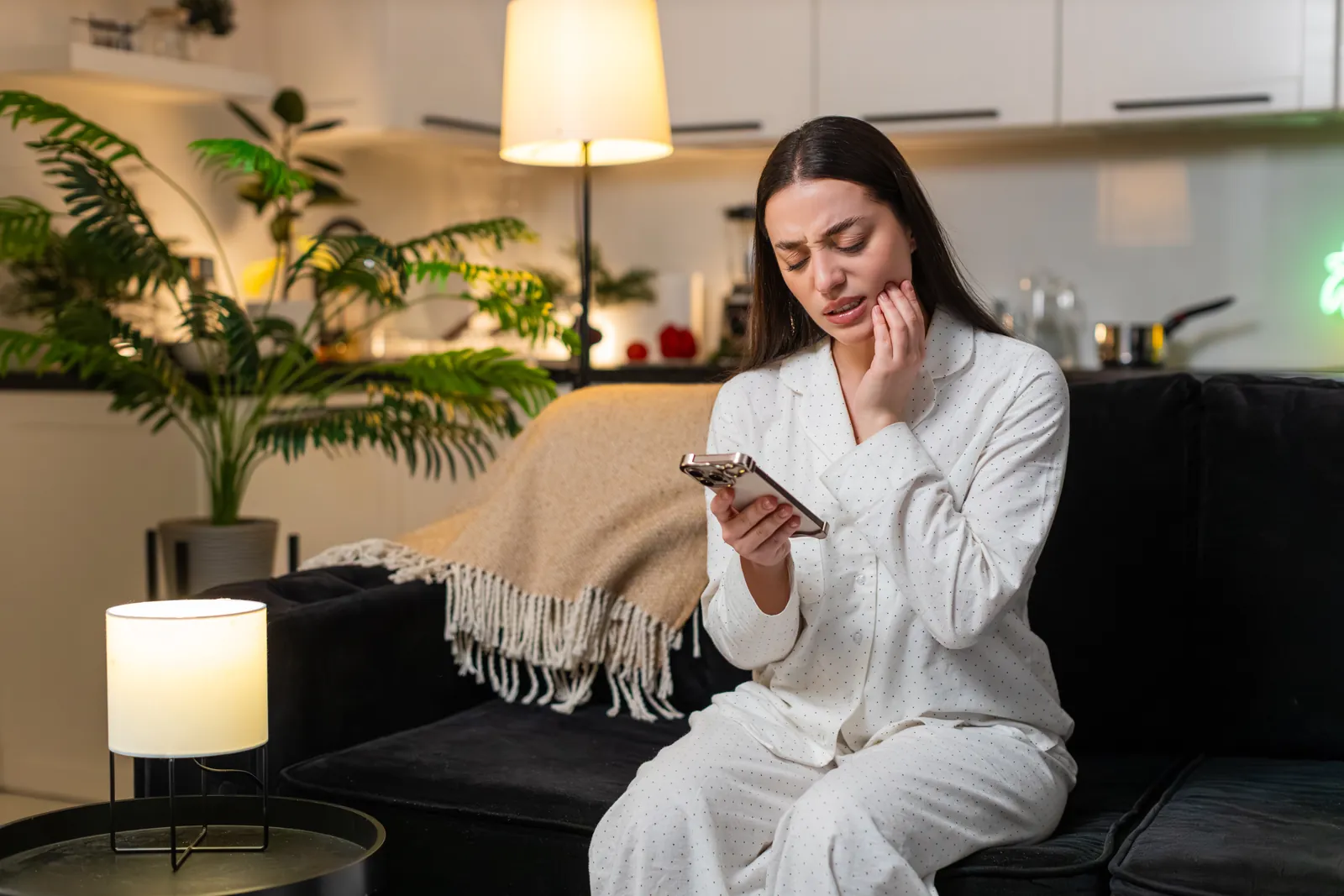 Woman at night holding her cheek while searching for a dentist on her phone
