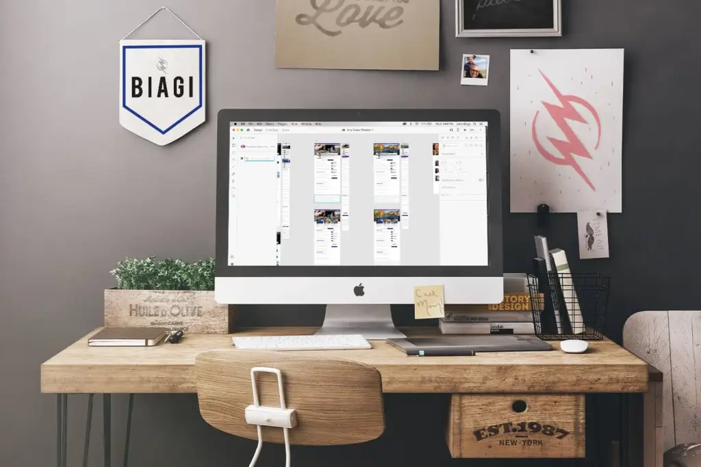A designer workspace with an iMac showing a page layout, a pennant reading BIAGI on the wall and a Wonderboy bolt print beside it